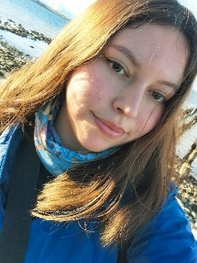 Gabriela Molina-Maldonado, a young woman with long brown hair, wearing a scarf, jacket and sweatshirt, with a rocky short behind her. 